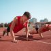 Two athletes doing push-ups on a track during daytime workout session outdoors.